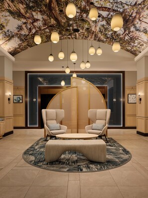 A lobby with a round seating area, hanging pendant lights, and a wall with a tree mural. - Tempo By Hilton Savannah Historic District (Savannah)