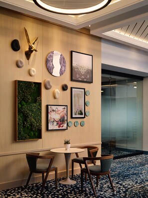 Un moderno vestíbulo de hotel con una mesa redonda, cuatro sillas y diversas obras de arte en la pared, incluyendo una cabeza de ciervo, pinturas abstractas y platos decorativos.