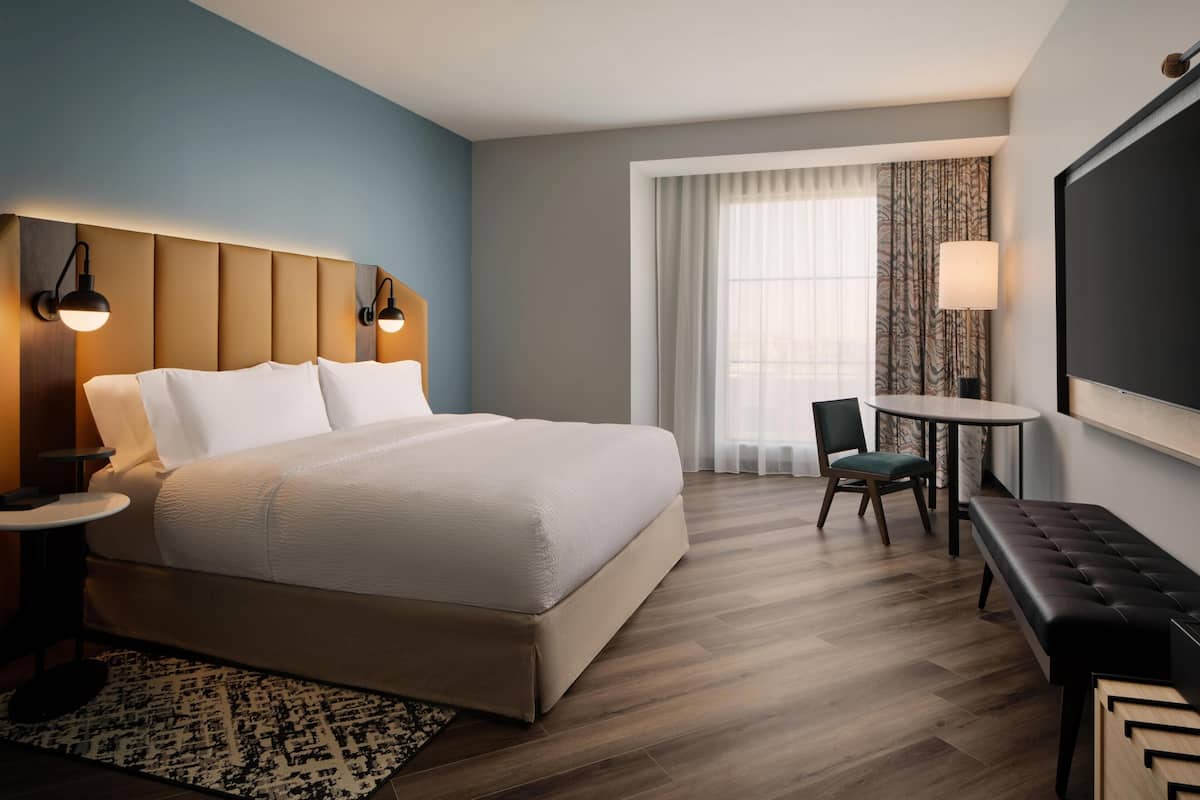 A hotel room with a large bed, a desk with a chair, a TV, and a window with curtains.