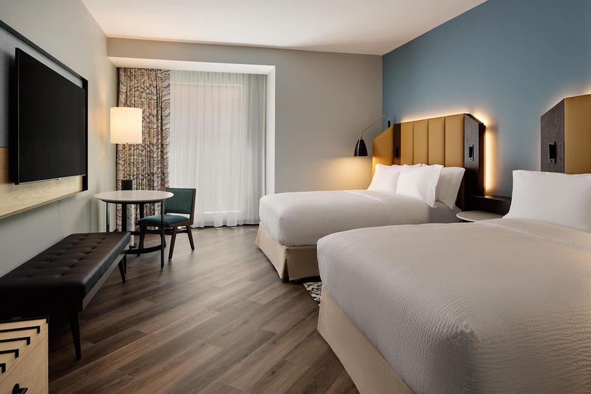 Habitación de hotel con dos camas, televisión, escritorio con silla y ventana con cortinas.