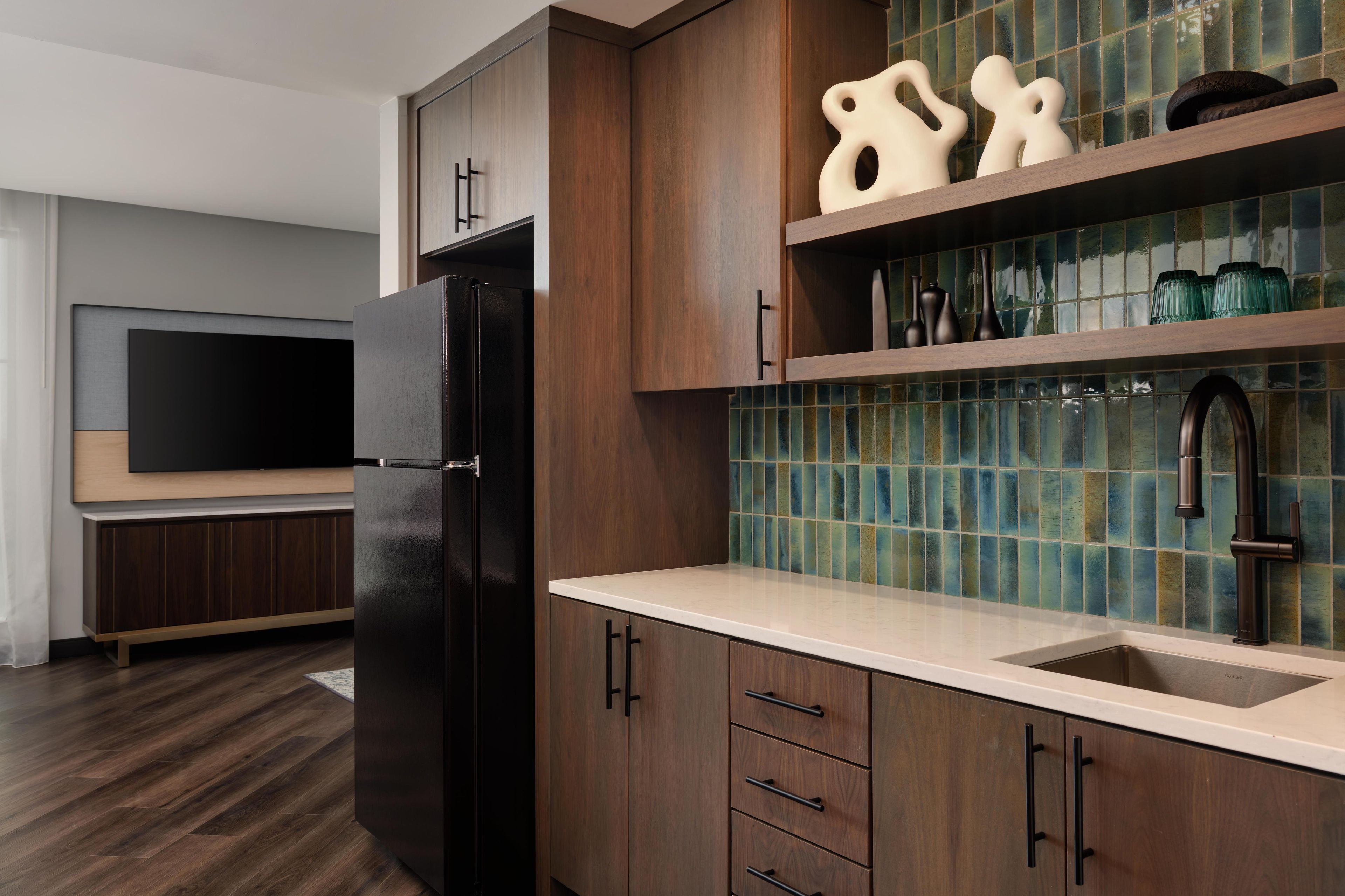 A modern kitchen with wooden cabinets, a black refrigerator, a tiled backsplash, and a built-in TV.