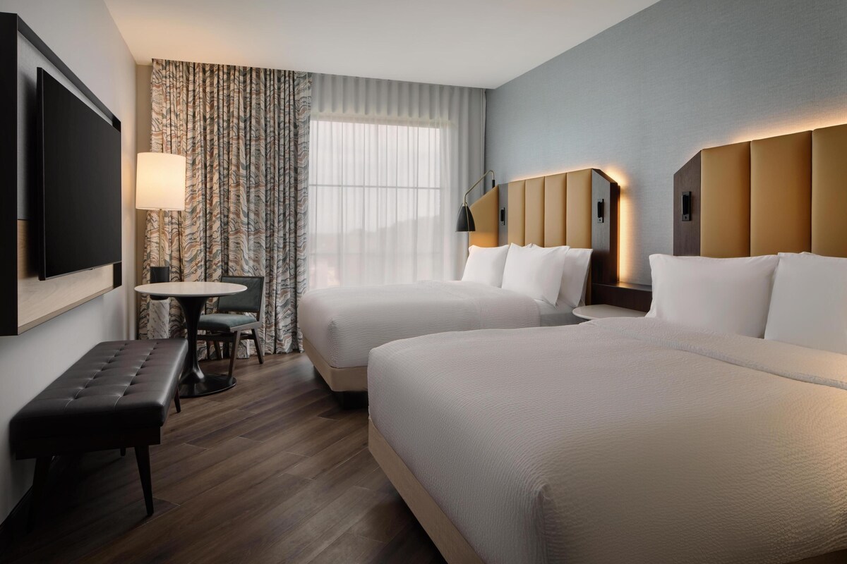 Une chambre d’hôtel avec deux lits, une télévision, un bureau avec une chaise et un banc.