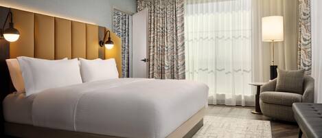 Ein Hotelzimmer mit einem großen Bett, einem Sessel, einem kleinen Tisch und einer Lampe.