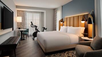 A hotel room with a large bed, a desk, a chair, a television, and a wall-mounted lamp.