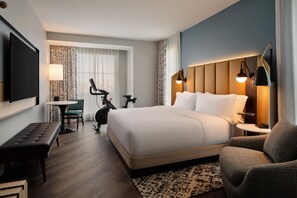 Ein Hotelzimmer mit einem großen Bett, einem Schreibtisch, einem Sessel, einem Fernseher und einer Wandleuchte.