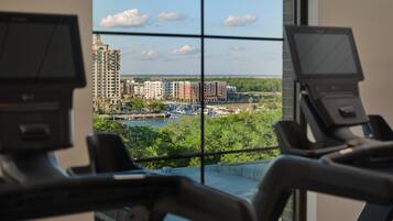 Ein Fitnessstudio mit Trainingsgeräten und Blick auf eine Stadtlandschaft durch große Fenster.