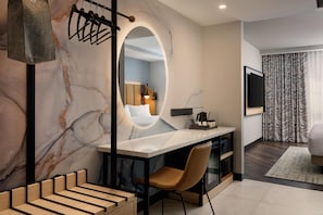 Habitación de hotel moderna con pared de mármol, un espejo grande, un escritorio con silla, un televisor montado en la pared y una cortina estampada.