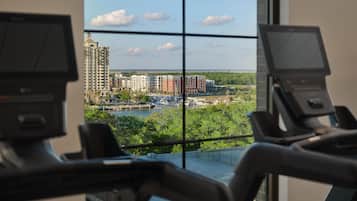 Un gimnasio con equipamiento de ejercicio y vistas a un paisaje urbano a través de amplios ventanales.