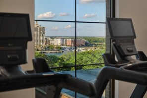 Un gimnasio con equipamiento de ejercicio y vistas a un paisaje urbano a través de amplios ventanales.