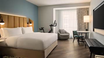A hotel room with a large bed, a desk with a chair, a treadmill, and a TV.