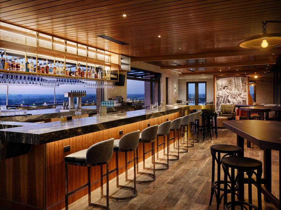A bar area with a long counter, multiple stools, and a view of the cityscape.