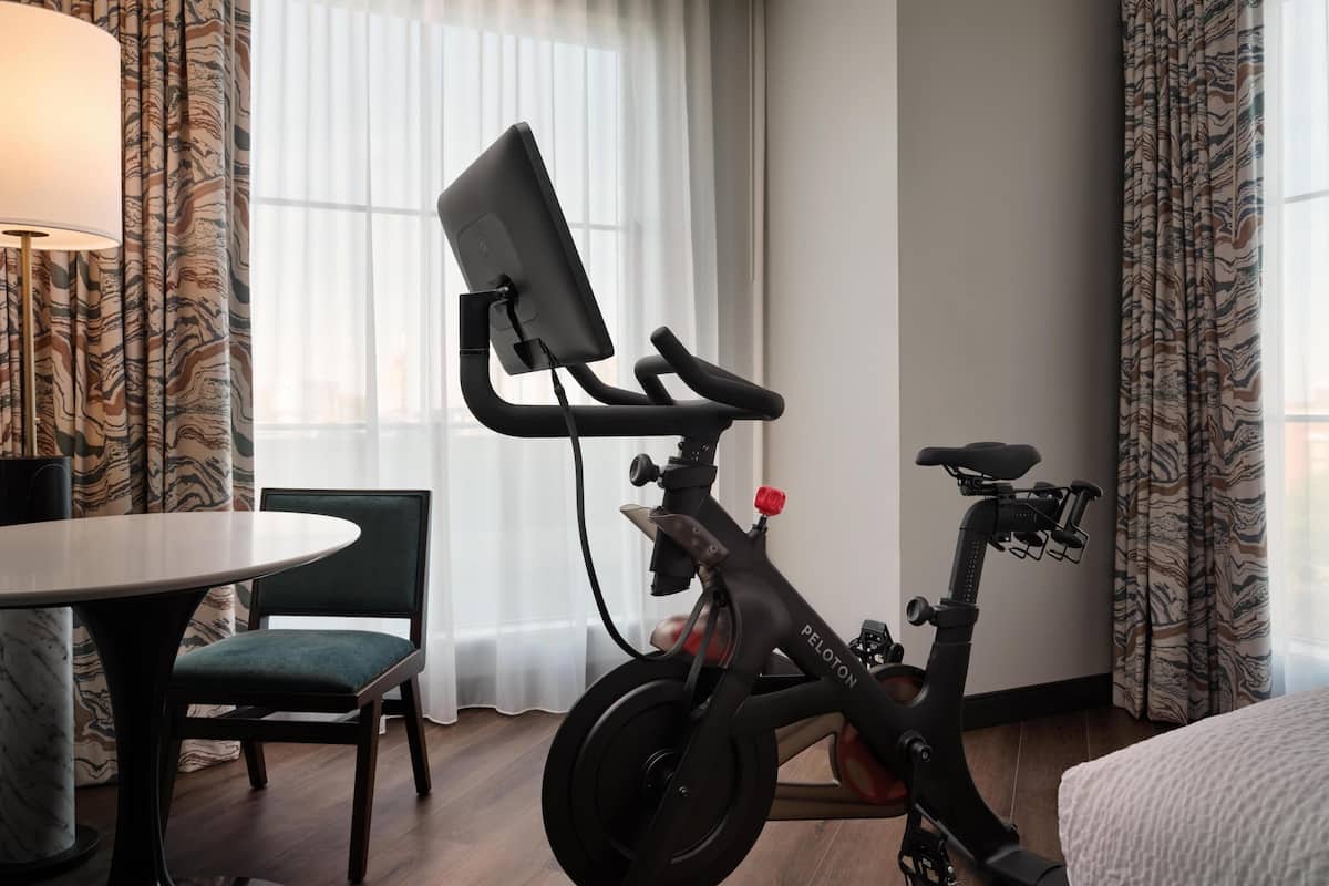 A room with a desk, chair, and an exercise bike with a screen.