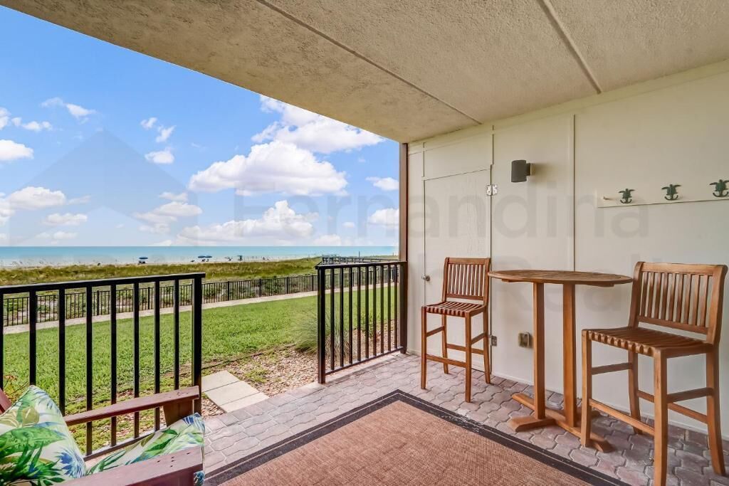 Een balkon met uitzicht op het strand, twee houten stoelen, een klein tafeltje en een deurmat.