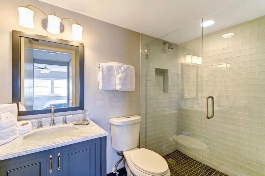 A bathroom with a glass-enclosed shower, a sink with a mirror, and a toilet.