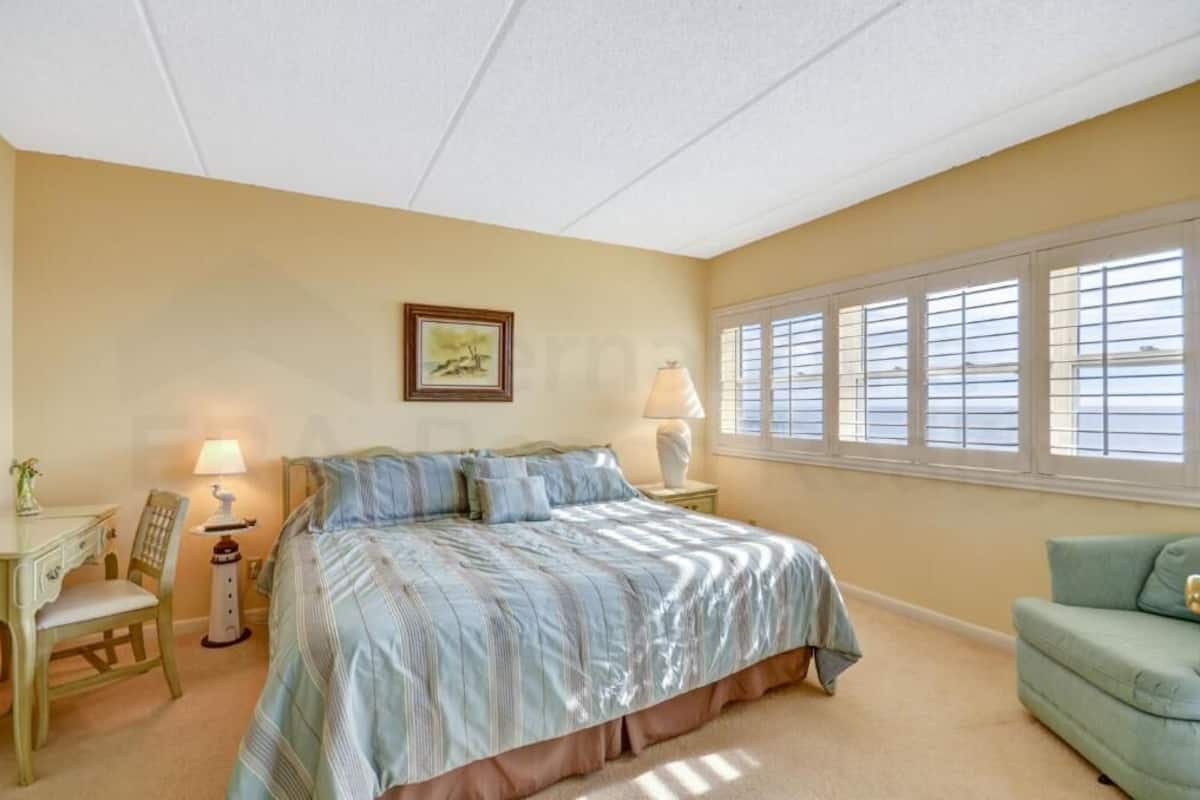 A bedroom with a bed, a desk, a chair, a lamp, and a window with blinds.