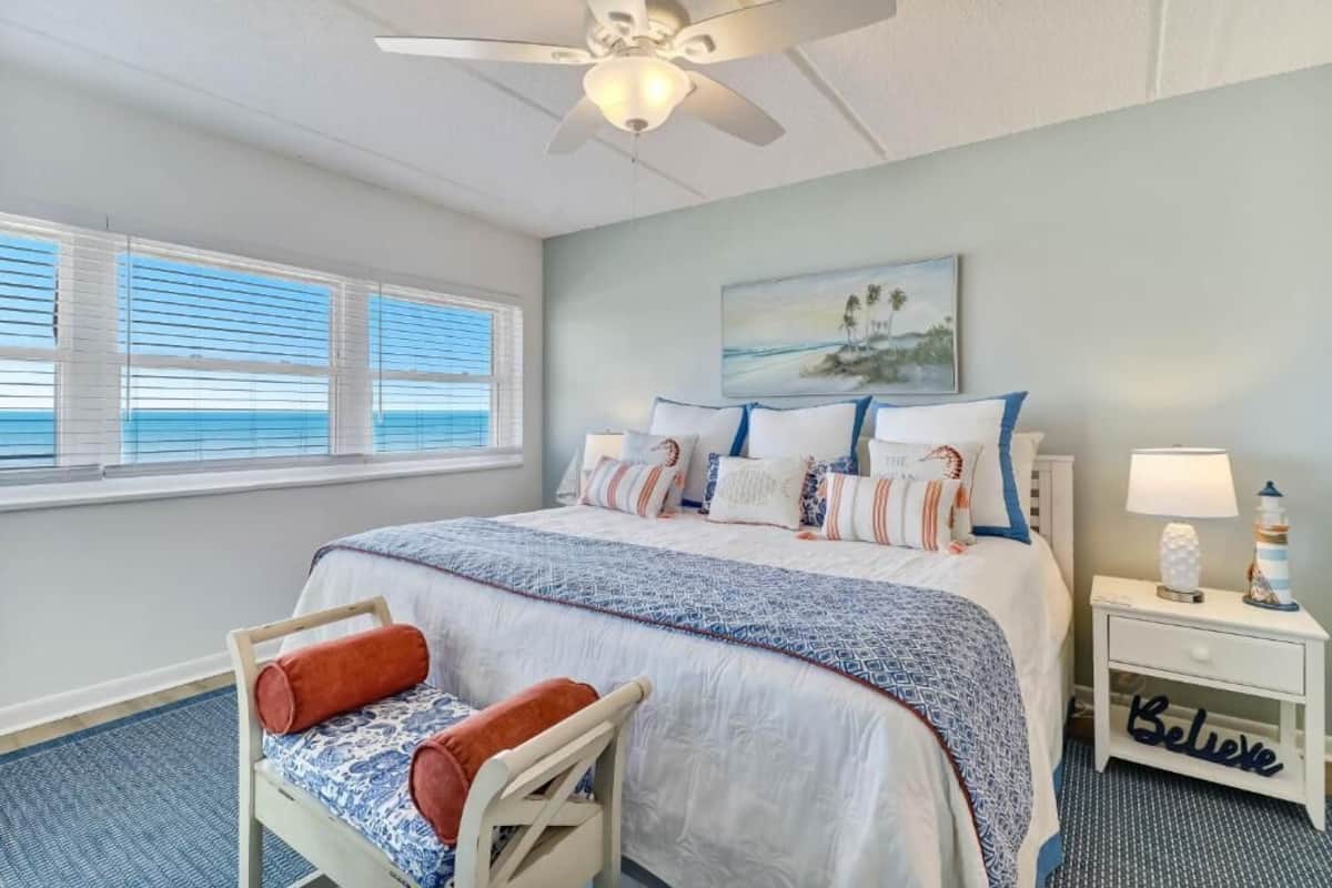 A bedroom with a bed, a chair, a nightstand, a lamp, and a ceiling fan.