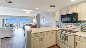 Une cuisine moderne avec des armoires blanches, un grand îlot central et une vue sur l’extérieur.