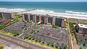 Vue aérienne d’un hôtel avec un parking, une plage et l’océan en arrière-plan.