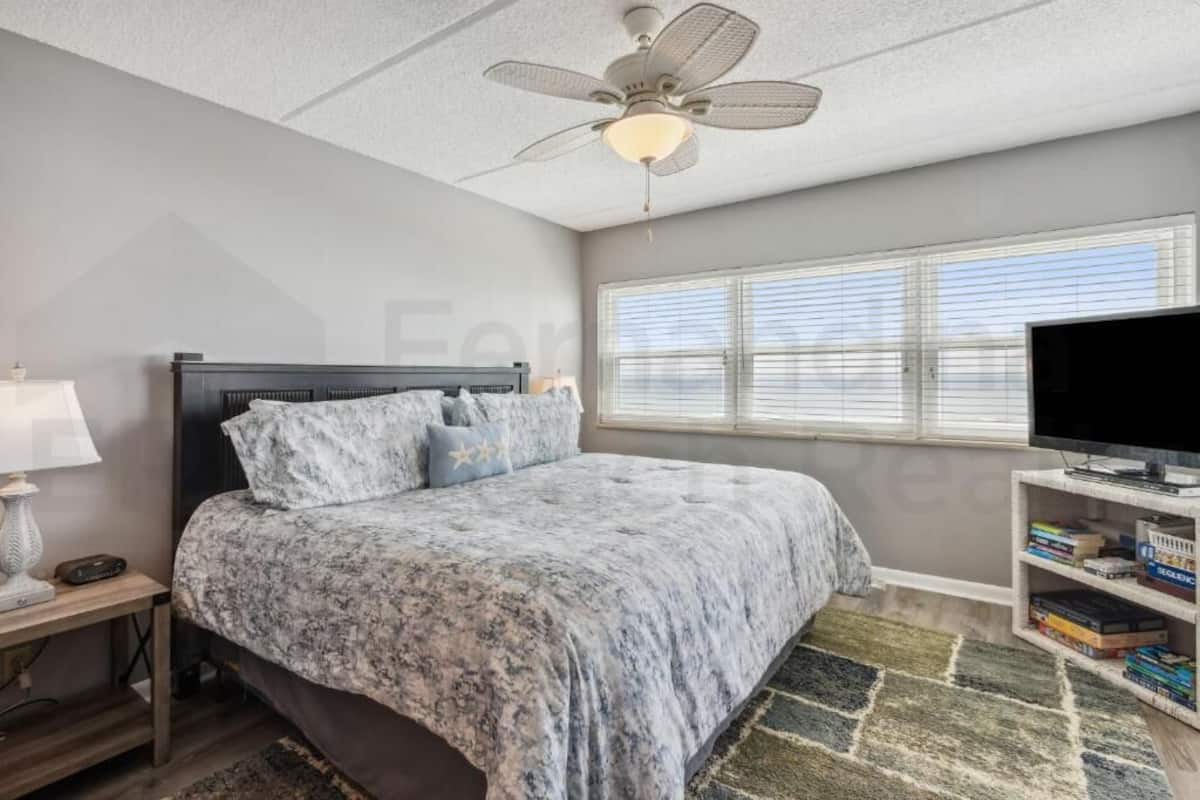 A bedroom with a bed, a ceiling fan, a TV, and a bookshelf.