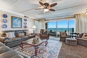 A spacious living room with a leather sofa, a glass coffee table, and a view of the ocean through large windows. - Amelia by the South (Fernandina Beach)