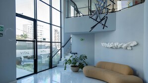 Un lobby moderno con entrada de vidrio, una escalera, una planta en maceta y un sofá color crema.