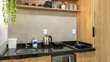 A kitchen with a granite countertop, a coffee maker, a kettle, a frying pan, and a microwave.