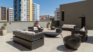 An outdoor patio with wicker furniture, potted plants, and a view of surrounding buildings. - Cozy Apartment Close to the Center Pgo309 (Poços de Caldas)