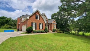 A two-story brick house with a front garage, a covered porch, and a well-maintained lawn. - Cozy, Very Large Studio Hideaway in a Peaceful Neighborhood (Loganville)