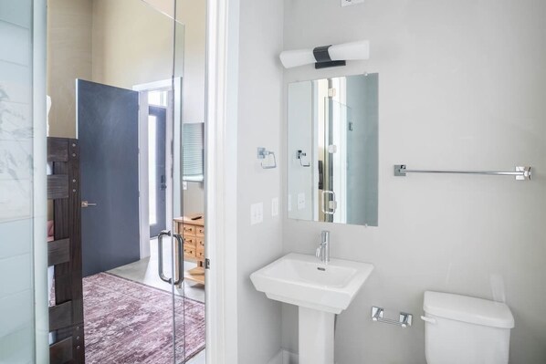 Un baño con lavamanos blanco, espejo y retrete.