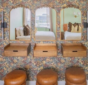 A room with three mirrors, a bed, a nightstand, and a wooden bench.
