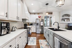 A modern kitchen with white cabinetry, stainless steel appliances, a coffee maker, and a hanging light fixture. - Family-Friendly 4BR | King Beds + Game Room (Bellevue)