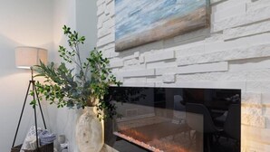 Una chimenea con frente de vidrio, una pared blanca con textura y un cuadro colgado encima.