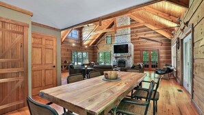 A spacious wooden cabin interior with a large dining table, multiple seating arrangements, and a stone fireplace.