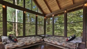 A cabin with large windows, wooden floors, and two benches with pillows.