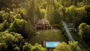 Ein großes Haus, umgeben von dichtem Wald, mit einem Pool und einer Auffahrt zum Eingang.