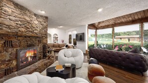 Una sala de estar acogedora con chimenea de piedra, asientos cómodos y grandes ventanales con vistas a un jardín.
