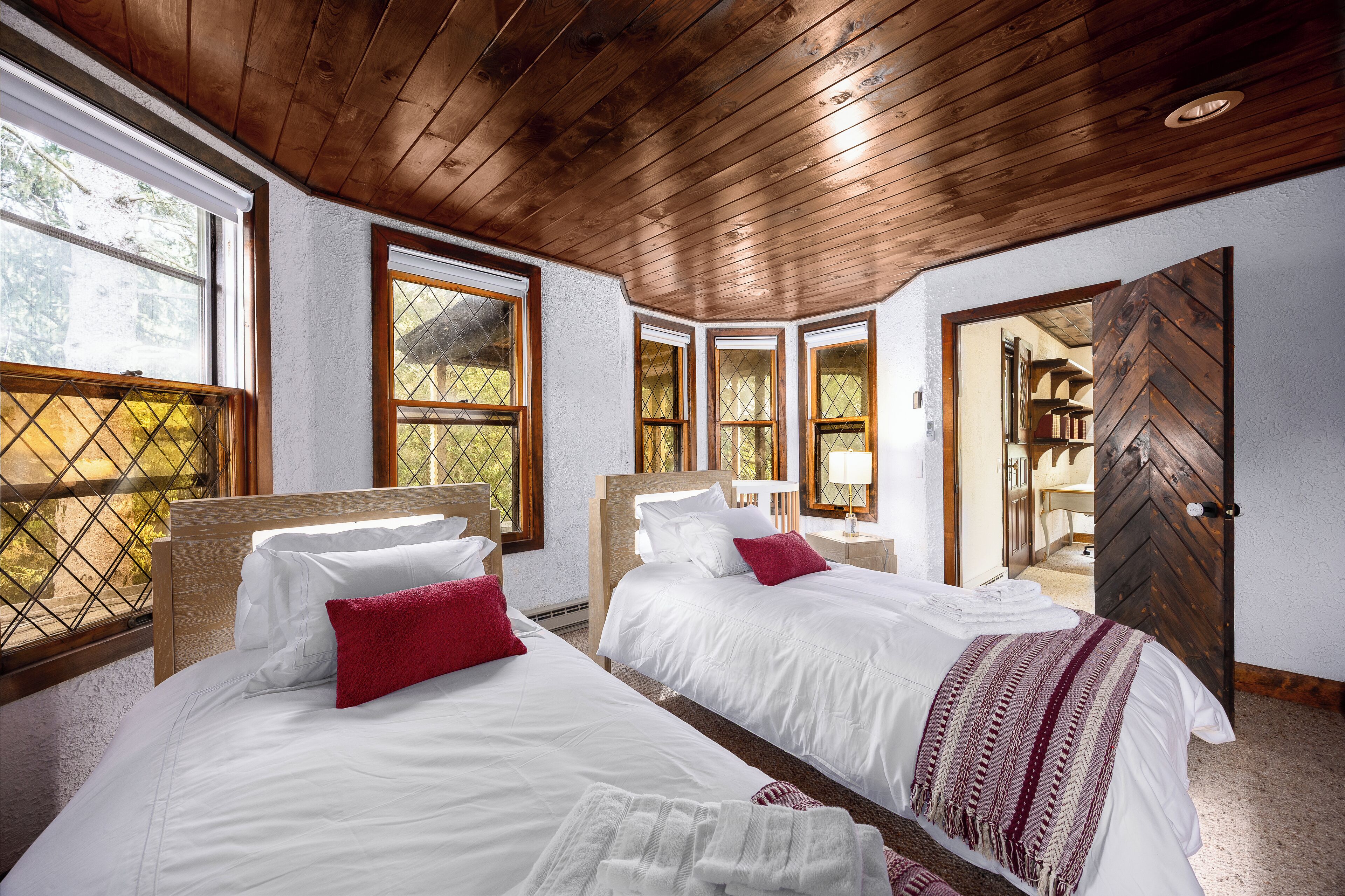 Ein Zimmer mit zwei Betten, Holzboden, großen Fenstern und Blick ins Freie.