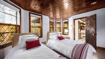Ein Zimmer mit zwei Betten, Holzboden, großen Fenstern und Blick ins Freie.