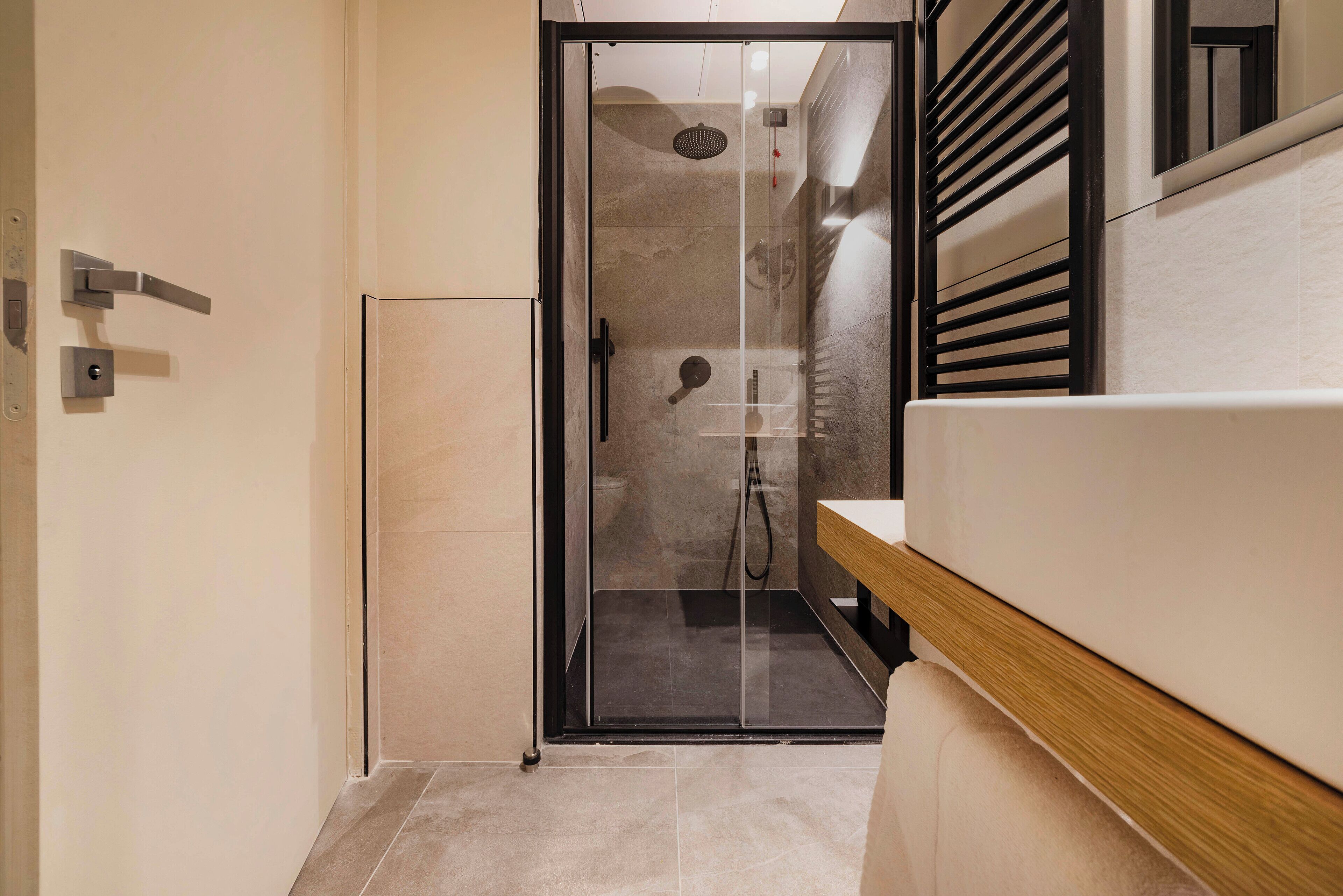 Un bagno moderno con cabina doccia in vetro, mobile lavabo in legno e porta asciugamani a parete.