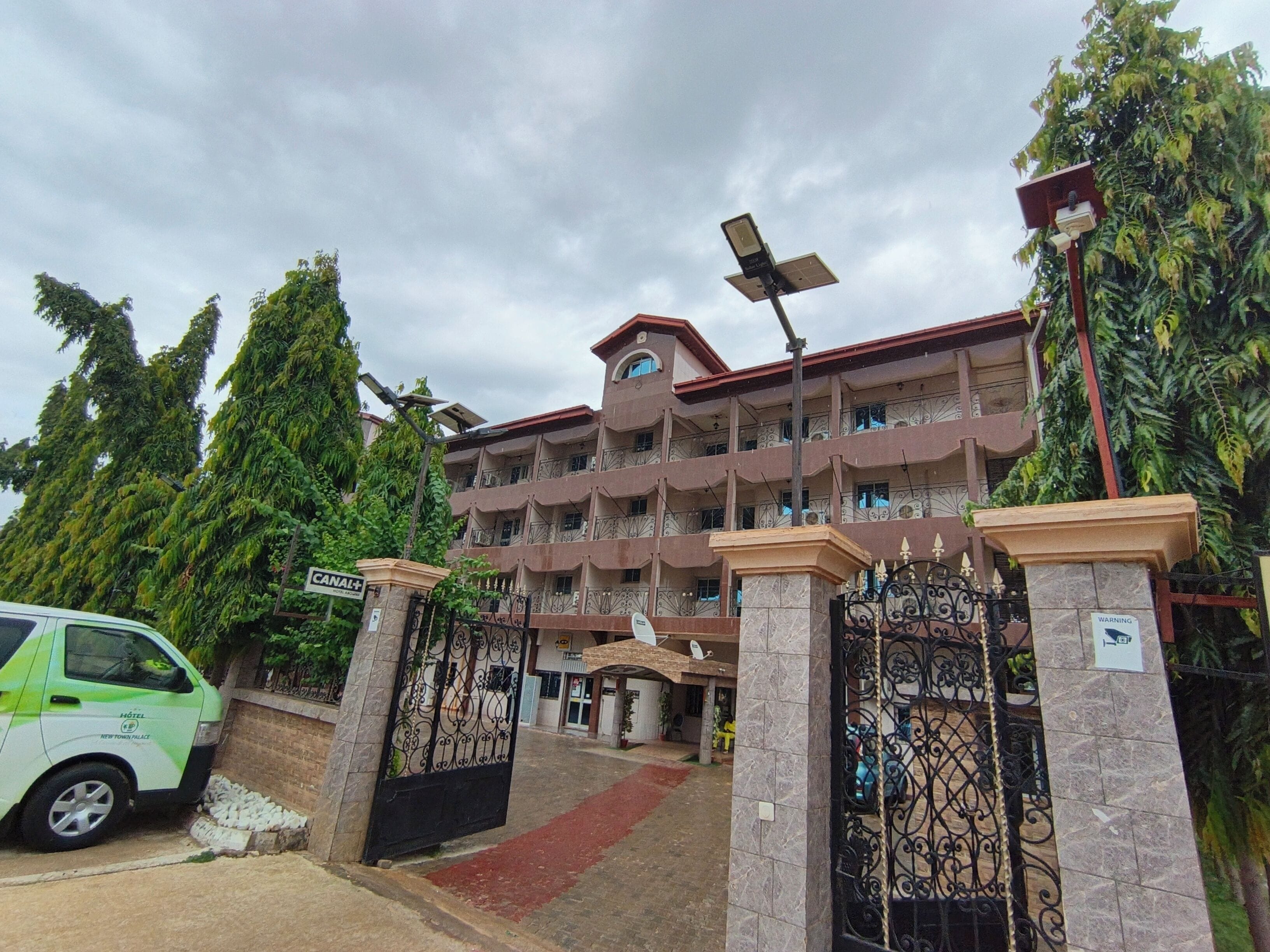 A multi-story hotel with a gated entrance, solar panels, and lush greenery around.