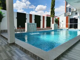 Piscina con fuente de agua, rodeada por un edificio moderno con suelo de baldosas y cielo despejado.