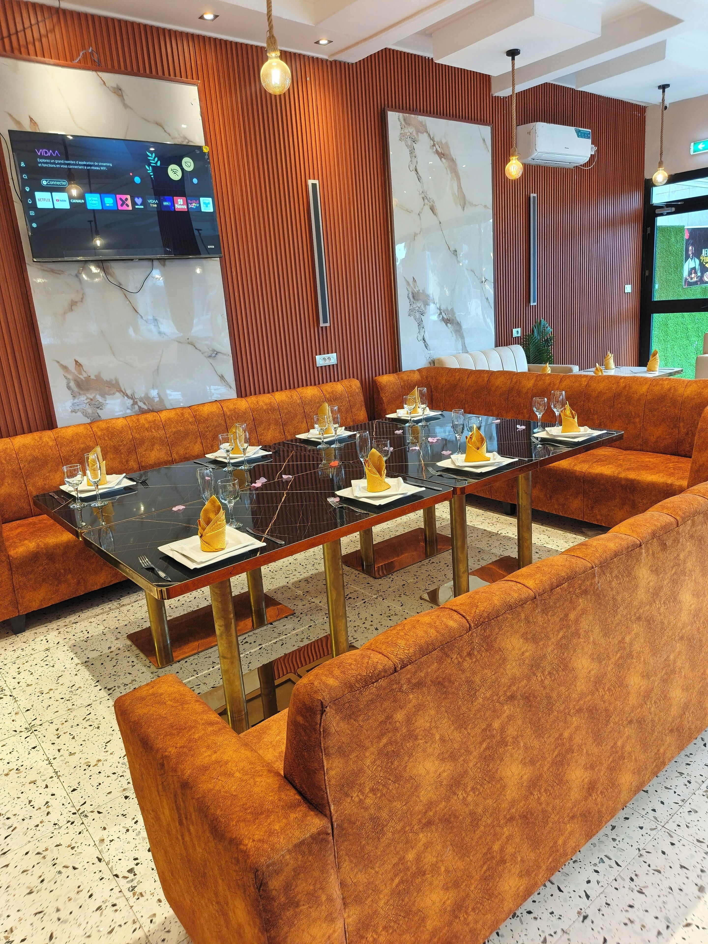 Un comedor moderno con asientos tapizados en naranja, mesas negras y detalles dorados.