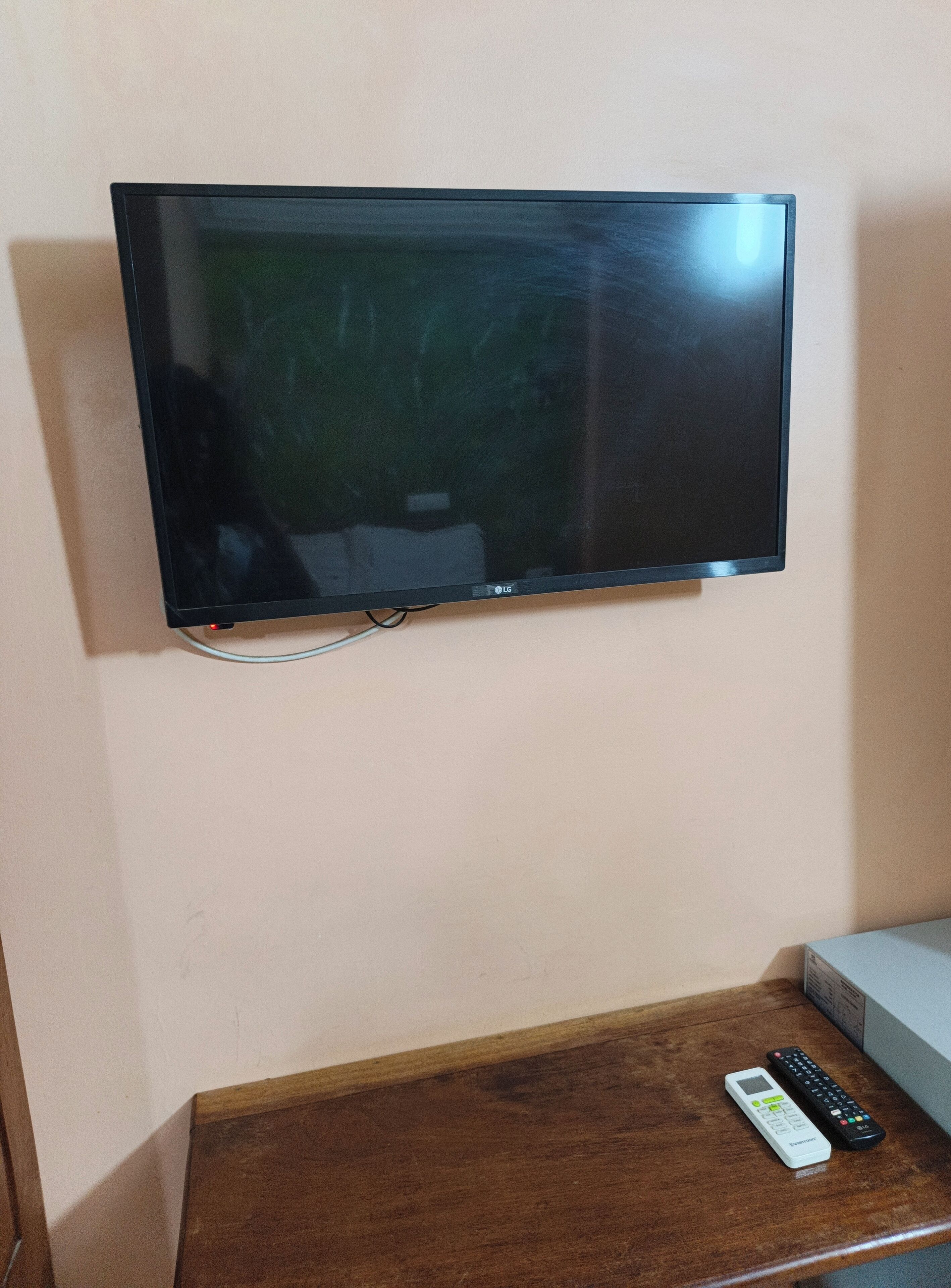 A flat-screen TV mounted on a wall, a wooden table with a remote control, and a cable box.