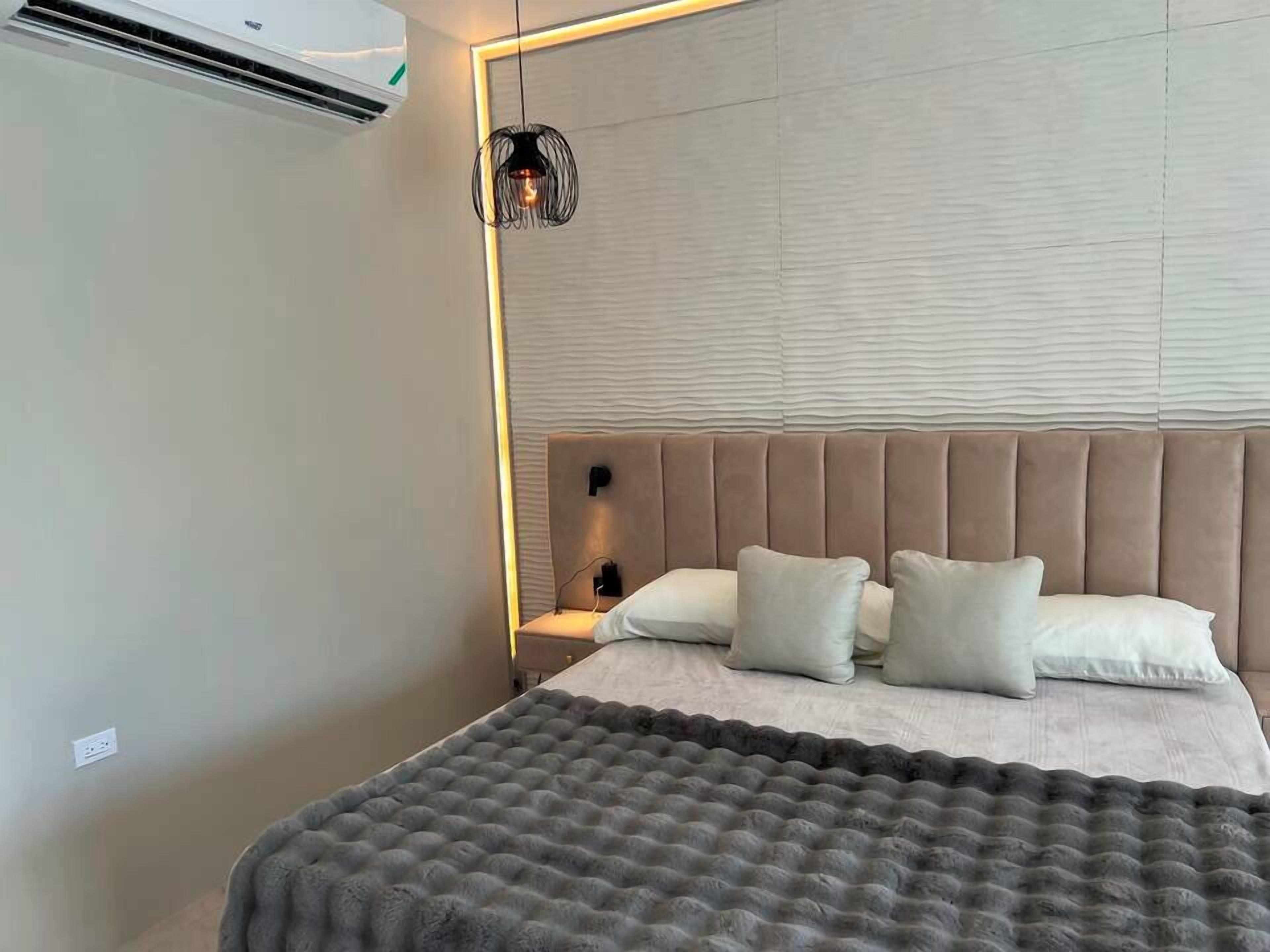 Un dormitorio moderno con un cabecero capitonado, una manta gris y una lámpara colgante.
