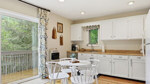 Una cucina con mobili bianchi, un tavolo da pranzo con sedie, una finestra che si affaccia sul verde e una ventola a soffitto.