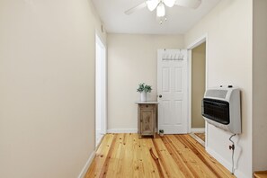 A hallway with wooden flooring, a white door, a small cabinet with a plant, and a wall-mounted air conditioning unit.