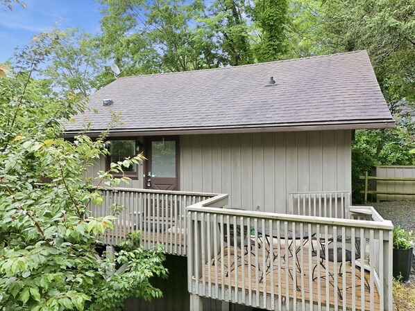 A small, single-story cabin with a deck, surrounded by trees.