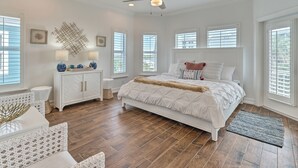 A bedroom with a large bed, a ceiling fan, and multiple windows with blinds.