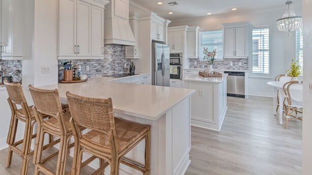 A modern kitchen with white cabinetry, a large island with bar stools, and a chandelier.