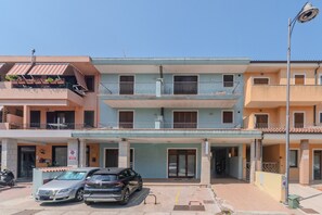 Un edificio de varios pisos con balcones, un coche estacionado al frente y un cielo despejado.